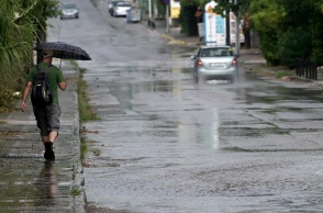 Πολίτης με ομπρέλα σε πεζοδρόμιο και δίπλα του αυτοκίνητο διασχίζει πλημμυρισμένο δρόμο