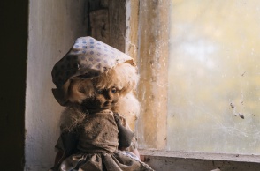 Λερωμένη και ταλαιπωρημένη κούκλα σε σκονισμένο παράθυρο