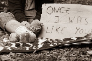 Άστεγος με τρύπια και βρώμικα ρούχα με χαρτόνι στο οποίο γράφει «Κάποτε ήμουν σαν εσένα»