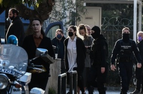 Η Ρούλα Πισπιρίγκου με λευκό πουκάμισο και μαύρο πανωφόρι οδηγείται στην ανακρίτρια