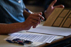 Το τετράδιο απαντήσεων για τα θέματα των Νέων Ελληνικών στα οποία εξετάστηκαν τα ΕΠΑΛ - Οι κόλλες με τα θέματα και στιλό πάνω στο θρανίο - Διακρίνεται το χέρι υποψηφίου