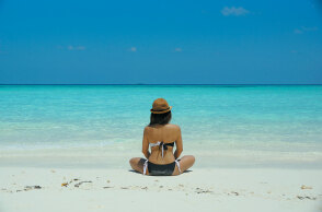 Κοπέλα με μαγιό κάθεται σε αμμώδη παραλία