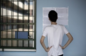 Μαθητής μπροστά από αναρτημένες κόλλες Α4 σε τοίχο σχολείου με τις βαθμολογίες των υποψηφίων στις Πανελλήνιες 2023