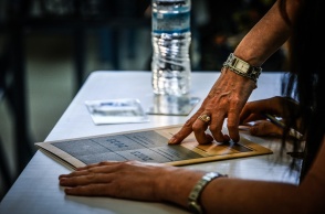 Χέρι επιτηρητή και υποψήφιας των Πανελληνίων 2023 πάνω από το τετράδιο απαντήσεων
