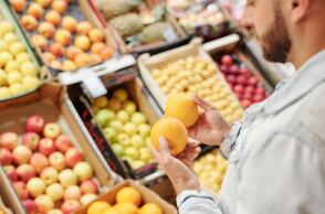 Άνδρας κρατά πορτοκάλια μπροστά από τον τομέα με φρούτα και λαχανικά σε σούπερ μάρκετ