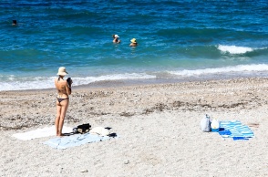 Γυναίκα σε παραλία όρθια κοντά στην απλωμένη πετσέτα της - παραλία με λίγο κυματάκι