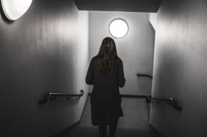 Γυναίκα γυρισμένη πλάτη σε σκοτεινό διάδρομο - Εικόνα που παραπέμπει σε κακοποίηση και μυστήριο