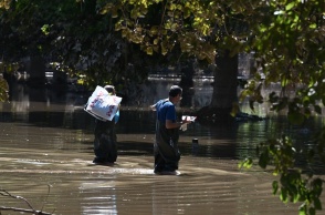 Άνδρες με προστατευτικά περπατούν σε πλημμυρισμένο δρόμο και κουβαλούν πράγματα