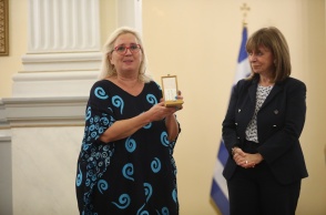 Η Μαρία Τσιαλέρα κρατά στα χέρια τον Αργυρό Σταυρό του Τάγματος της Ευποιΐας και στέκεται συγκινημένη δίπλα στην Πρόεδρο της Δημοκρατίας, Κατερίνα Σακκελαροπούλου