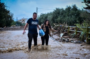 Γυναίκα και άνδρας βοηθούν ο ένας τον άλλο να περπατήσουν σε πλημμυρισμένο δρόμο στην Αγριά της Μαγνησίας
