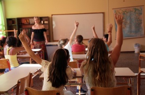 Εκπαιδευτικός σε σχολική αίθουσα με παιδιά που σηκώνουν το χέρι τους για να πουν μάθημα