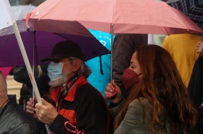 Γυναίκα με ομπρέλα φορά μάσκα δίπλα σε άνδρα επίσης με μάσκα και ομπρέλα