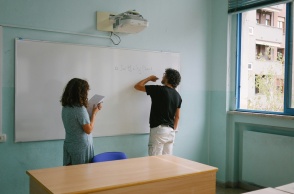 Μαθήτρια και καθηγητής σε τάξη γράφουν στον πίνακα