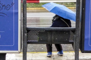 Γυναίκα με ομπρέλα σε στάση λεωφορείου ενώ βρέχει