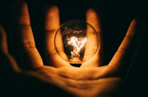 Αναμμένη λάμπα ανάμεσα στα δάχτυλα ενός χεριού