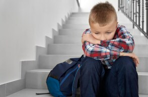 Παιδί κάθεται στα σκαλιά με την τσάντα του δίπλα και έχει ακουμπήσει το κεφάλι του στα γόνατά του - Εικόνα που παραπέμπει σε βία στα σχολεία - bullying