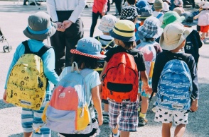 Παιδιά με καλοκαιρινά ρούχα και τσάντες στην πλάτη περπατούν πιασμένα χεράκι - χεράκι