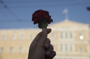 Χέρι κρατά κόκκινο τριαντάφυλλο με φόντο τη Βουλή των Ελλήνων