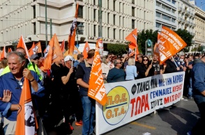 Άτομα που συμμετέχουν σε συγκέντρωση στο κέντρο της Αθήνας κρατώντας σημαίες και πανό της ΠΟΕ-ΟΤΑ