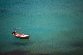 Παραλία και καΐκι αγκυροβολημένο που έχει στην πλώρη του την ελληνική σημαία