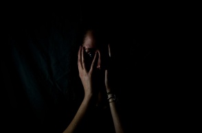 Γυναίκα που κλαίει κρατά το πρόσωπό της ενώ βρίσκεται στο ημίφως - Εικόνα που παραπέμπει σε κακοποίηση και ενδοοικογενειακή βία