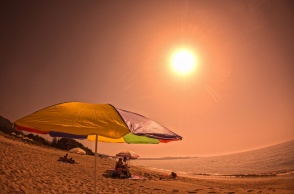 Ο ήλιος πάνω από παραλία όπου λουόμενοι έχουν βάλει ομπρέλα