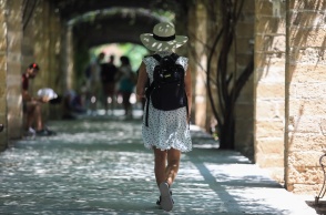 Γυναίκα με καπέλο και καλοκαιρινά ρούχα περπατά στον Εθνικό Κήπο