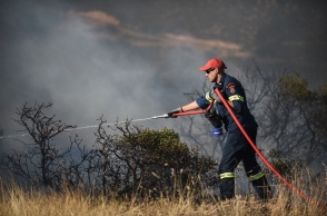 Πυροσβέστης με μάνικα ρίχνει νερό σε περιοχή όπου έχει περάσει φωτιά για τον κίνδυνο αναζωπυρώσεων