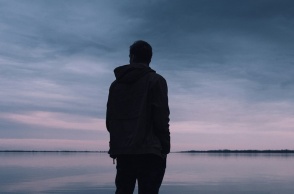 Νεαρό άτομο κοιτά τον ορίζοντα γυρισμένο πλάτη στον φακό