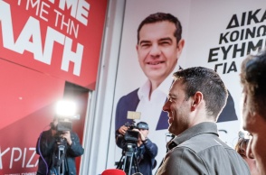 Ο Στέφανος Κασσελάκης προχωρά σε κτίριο που στο εξωτερικό του έχει αφίσα του ΑΛέξη Τσίπρα