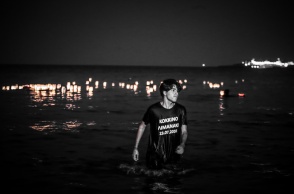 Νεαρό άτομο βγαίνει από τη θάλασσα όπου έχει αφήσει το φαναράκι του με μπλουζάκι που γράφει «Κόκκινο Λιμανάκι 23.07.2018»