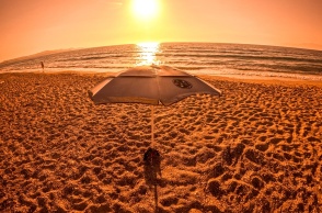 Φωτογραφία από παραλία εν μέσω καύσωνα με τον φακό να καταγράφει τον ήλιο και ομπρέλα σε παραλία