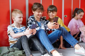 Παιδιά με κινητά καθισμένα στο πάτωμα διαδρόμου σχολείου