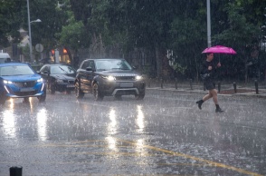 Γυναίκα με ομπρέλα διασχίζει δρόμο υπό καταρρακτώδη βροχή