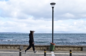Κοπέλα περπατά με ζακέτα σε παραλιακό μέρος με πολύ αέρα