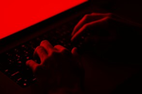 Άτομο σε σκοτεινό κόκκινο φόντο πληκτρολογεί - Εικόνα που παραπέμπει στη δράση χάκερ