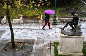 Γυναίκα με ομπρέλα περπατά δίπλα από άγαλμα στην Αθήνα