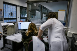 Γυναίκα σε υπολογιστή στην υπηρεσία της και από πάνω της μία άλλη γυναίκα που της δίνει οδηγίες