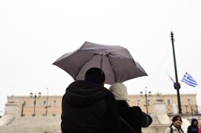 Πολίτες με ομπρέλα προστατεύονται από τη βροχή μπροστά από τη Βουλή