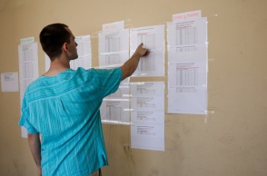 Άτομο μπροστά από τις βαθμολογίες των μαθημάτων των Πανελληνίων που είναι ανηρτημένες έξω από σχολείο