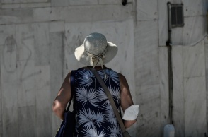 Γυναίκα με γυρισμένη πλάτη στον φακό και τη μάσκα προστασίας από τον κορωνοϊό αφημένη στον αγκώνα