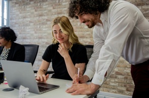 Εργαζόμενος κοιτά σε υπολογιστή πάνω από άλλη εργαζόμενη που κοιτά σε υπολογιστή