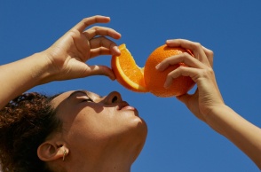 Κοπέλα στον ήλιο με κομμένο πορτοκάλι πάνω από το πρόσωπό της