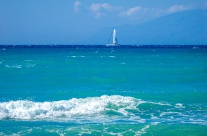 Κυματάκια σε παραλία και στο βάθος ένα ιστιοφόρο