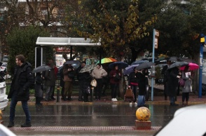 Πολίτες σε στάση λεωφορείου περιμένουν έχοντας ανοιχτή την ομπρέλα τους