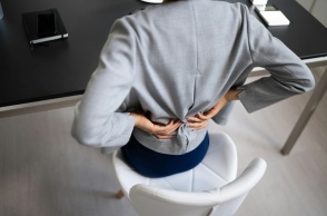 Εργαζόμενη κάθεται σε καρέκλα γραφείου και κρατά τη μέση της που φαίνεται ότι πονά