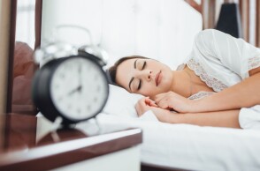 Γυναίκα κοιμάται στο κρεβάτι έχοντας στο κομοδίνο ένα ξυπνητήρι