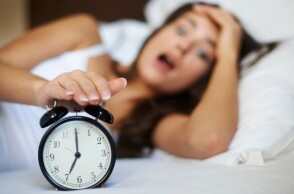 Γυναίκα ξυπνά το πρωί και πιάνει το ξυπνητήρι στο κρεβάτι