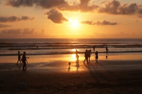 Λουόμενοι σε παραλία με φόντο το ηλιοβασίλεμα