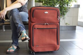 Επιβάτης με σαγιονάρα δίπλα σε βαλίτσα ετοιμάζεται για καλοκαιρινές διακοπές
